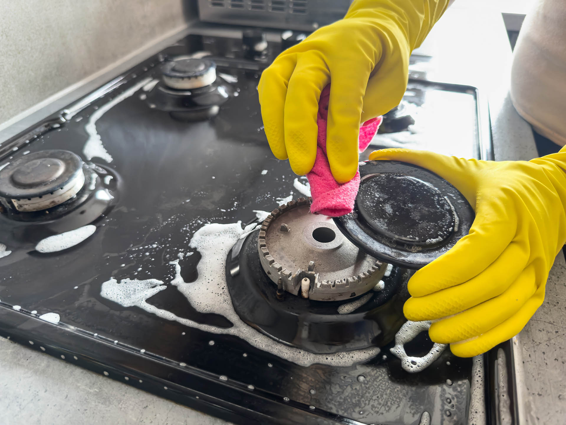 woman cleaning  sponge rag with white foam and detergent washing kitchen gas stove. House cleaning concept